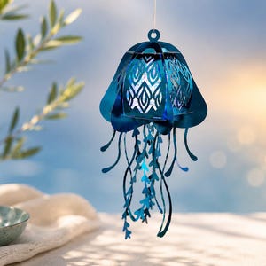May include: A hanging jellyfish ornament crafted from metallic blue material, featuring a bell-shaped top with intricate laser-cut patterns and multiple dangling, ribbon-like tentacles that extend downward from the central structure.