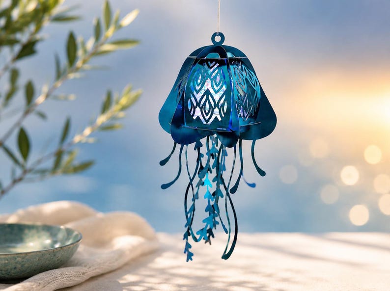 May include: A hanging jellyfish ornament crafted from metallic blue material, featuring a bell-shaped top with intricate laser-cut patterns and multiple dangling, ribbon-like tentacles that extend downward from the central structure.