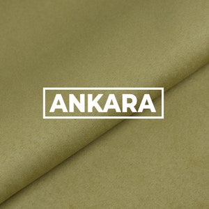 Può includere: Primo piano di un pezzo di tessuto piegato in un colore verde tenue. Il tessuto ha una superficie testurizzata e la parola "ANKARA" è stampata in bianco sul tessuto.