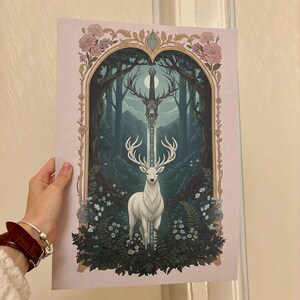 May include: A fantasy art print featuring a white stag with large antlers, standing before a forest scene. A sword is positioned above the stag. The artwork is framed by floral and ornate arch details, with a soft pink background.