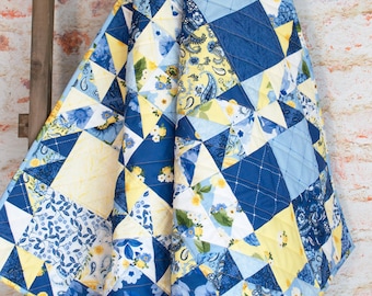May include: A blue and yellow patchwork quilt with a floral pattern. The quilt is made of various fabrics and is stitched together in a geometric pattern.