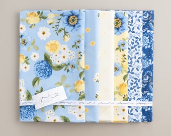May include: A set of six fabric squares featuring floral patterns in shades of blue and yellow. The fabrics are arranged in a row, with the text "Just keep sewing" printed on a white ribbon.