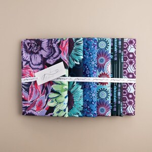 May include: A set of eight fabric squares with various colorful patterns, including floral, geometric, and abstract designs. The fabrics are arranged in a row and tied together with a white ribbon. The ribbon has the text "Just Keep Sewing" printed on it.