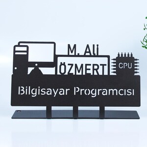 Può includere: Un cartello in metallo nero con un monitor di computer, un chip CPU e il testo "M. Ali Özmert Bilgisayar Programcısı".