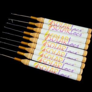 Peut inclure: Un ensemble de dix crochets à crochet avec des manches en bois et des pointes en métal doré. Les manches sont blanches avec le texte "SOLARLOCS" imprimé en rose, jaune et orange.