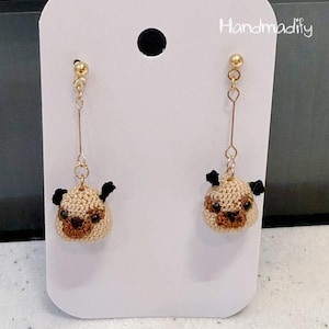 May include: A pair of handmade earrings featuring a pug design. The earrings are made of beige and brown crochet with black accents. The earrings hang from gold-colored posts. The text "Handmadify" is visible on the white card.