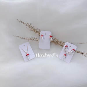 Könnte beinhalten: Eine Sammlung handgefertigter Schmuckstücke mit Pilzmotiven, darunter eine Halskette, Ohrringe und eine Ansammlung von Pilzanhängern. Die Pilze haben rote Kappen und weiße Stiele. Der Markenname "Handmadify" ist sichtbar.