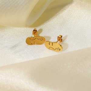 May include: A pair of gold-tone earrings with a unique abstract design. The earrings are made of metal and have a post back closure.