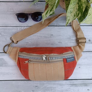 May include: A tan and red fanny pack with two zipped compartments and a silver zipper pull. The bag has a tan adjustable strap and the text "Anna Shaffer" is printed on the front.