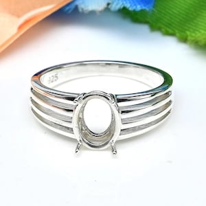 May include: A silver ring with a 925 stamp, featuring a wide band with three parallel lines and an oval-shaped setting for a gemstone.