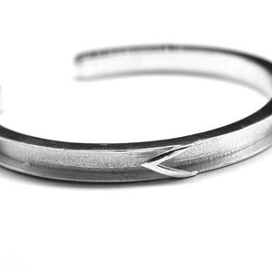 May include: A silver bangle bracelet with a textured finish and a subtle arrow design.