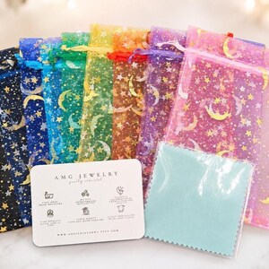 May include: A collection of sheer organza drawstring pouches in black, blue, green, yellow, orange, purple, and pink, each featuring a gold foil moon and star pattern. A white rectangular jewelry care card and a light blue polishing cloth are included.