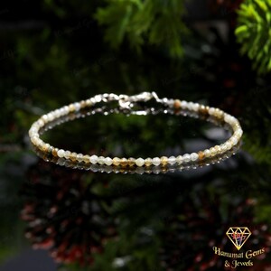 以下が含まれることがあります： 白、黄色、茶色の小さなファセット宝石をあしらった繊細なビーズブレスレット。 ブレスレットは細くてしなやかなコードに通されており、シルバーの留め金が付いています。 宝石の直径は約0.25cmです。