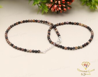 May include: A delicate necklace made with small, multi-colored gemstone beads. The beads are a mix of brown, black, and white, and are connected by a silver chain.