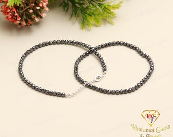 May include: A pair of black beaded anklets with a silver connector. The anklets are made of small, faceted black beads.