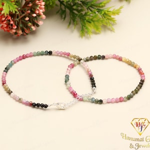 May include: Two delicate bracelets made of small, multi-coloured gemstone beads. The beads are pink, green, and black. The bracelets are connected by a silver clasp.