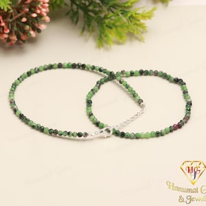 Puede incluir: Un collar de cuentas de piedras preciosas verdes y negras con un cierre de plata. El collar está hecho de pequeñas cuentas redondas y mide aproximadamente 45 cm de largo.