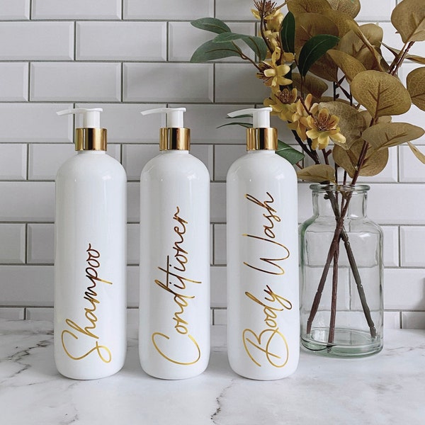 Set mit 3 eleganten weißen Shampoo-, Conditioner- und Body Wash Pumpflaschen mit glänzendem goldenem Schriftzug und Pumpe