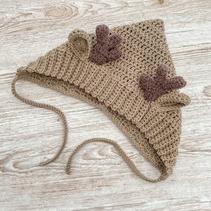 Op de afbeelding: Een bruine gehaakte hertenmuts met bruine viltgewei. De muts heeft een lange strik die onder de kin kan worden geknoopt.