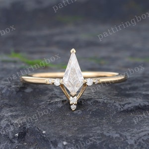 May include: A delicate gold ring featuring a single, large, clear, kite-shaped diamond. Smaller diamonds are set on the band, creating a geometric design.