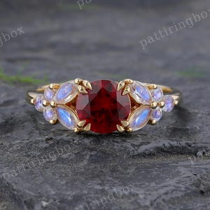 May include: A gold ring with a large, round, deep red gemstone at its centre, encircled by smaller, light blue gemstones. The ring's band is a simple gold design, highlighting the vibrant gemstones.
