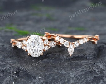 May include: A rose gold engagement ring set with a large oval-shaped center stone and smaller round stones. The matching wedding band features a delicate vine design with pear-shaped stones.