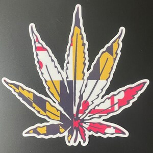 May include: A marijuana leaf sticker with the Maryland state flag design. The leaf is green with yellow, red, and white accents.