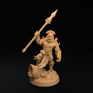 Könnte beinhalten: Eine hellbraune, unbemalte Miniaturfigur eines Kriegers in verzierter Rüstung, der einen Helm mit Kamm trägt und einen langen Speer hochhält. Die Figur steht in einer dynamischen Pose mit einem Fuß auf einem zylindrischen Objekt auf einem Sockel.