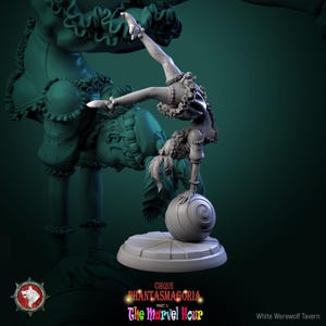 May include: A gray figurine of a circus performer balancing on a ball. The performer is wearing a ruffled outfit and a hat. The base of the figurine has the text "CIRQUE PHANTASMAGORIA PART 1: The Marvel Hour".