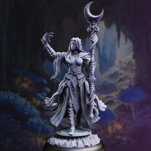 May include: A grey-toned fantasy figurine of a standing figure wearing layered robes and armour, holding a tall staff topped with a crescent moon. The figure has long hair, pointed ears, and one hand raised with swirling energy effects.