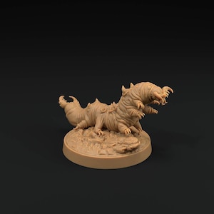 May include: A tan-coloured miniature figurine of a segmented, multi-legged creature with a curved tail and a head featuring multiple appendages and sharp mandibles, mounted on a circular base with a textured, rocky surface detail.
