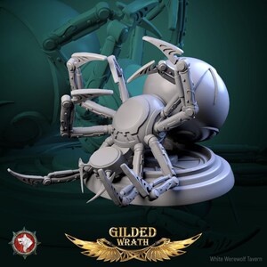 Puede incluir: Una figura de araña mecánica de color gris claro con patas articuladas segmentadas y un gran abdomen esférico, montada sobre una base circular. El texto GILDED WRATH aparece debajo de la figura con un emblema alado dorado y un logo de cabeza de lobo.