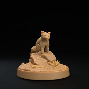 May include: A light tan, unpainted miniature figurine of a small fox-like creature sitting upright on a textured rock formation. The base is circular and smooth, providing a stable foundation for the detailed animal sculpture and rocky terrain.