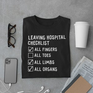 May include: A black t-shirt with a white graphic that says "Leaving Hospital Checklist" with checkboxes next to the following items: "All Fingers", "All Toes", "All Limbs", and "All Organs".