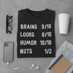 May include: Black t-shirt with white text that reads "BRAINS 9/10 LOOKS 8/10 HUMOR 10/10 NUTS 1/2".