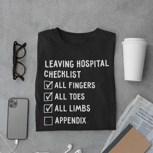 May include: Black t-shirt with a white checklist that says "Leaving Hospital Checklist" with checkboxes next to the following items: "All Fingers", "All Toes", "All Limbs", and "Appendix". The first three checkboxes are checked, while the last one is unchecked.