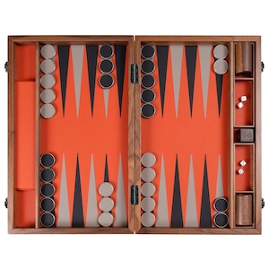 May include: A wooden backgammon game set with a walnut finish. The board is open and the playing surface is orange with black and gray triangles. The game pieces are black and gray and are arranged on the board. The set includes dice and a dice cup.
