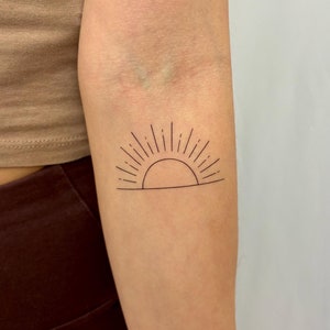 Può includere: Un semplice tatuaggio a linea di un'alba con raggi che emanano dal sole.
