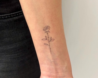 Könnte beinhalten: Ein einfaches Linien-Tattoo einer Rose mit Blättern und Stiel auf dem Handgelenk einer Person.