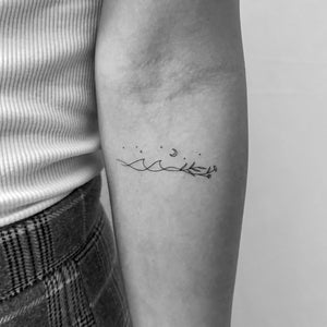 May include: A black and white line drawing tattoo of a wave, a crescent moon, stars, and a branch with leaves and flowers.