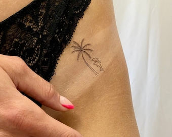 May include: A small tattoo of a palm tree with two dolphins jumping out of the water on a person's hip.