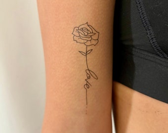 Könnte beinhalten: Schwarze Umrisstätowierung einer Rose mit Stiel und dem Wort "love" in Schreibschrift. Die Tätowierung befindet sich am Arm. Die Rose befindet sich am oberen Ende des Stiels.
