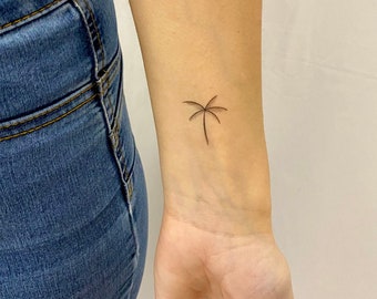 May include: A simple line drawing tattoo of a palm tree on a person's wrist.