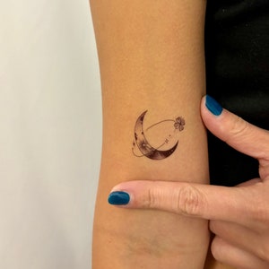 Peut inclure: Un tatouage temporaire en forme de croissant de lune avec une petite fleur et des étoiles.