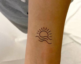 May include: A simple line drawing tattoo of a sun setting over the ocean. The sun is a circle with rays and the ocean is represented by two wavy lines.