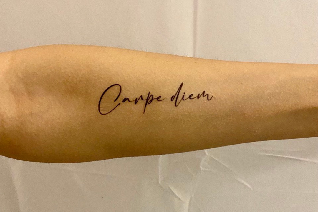 Carpe diem lettering tattoo located on the upper arm