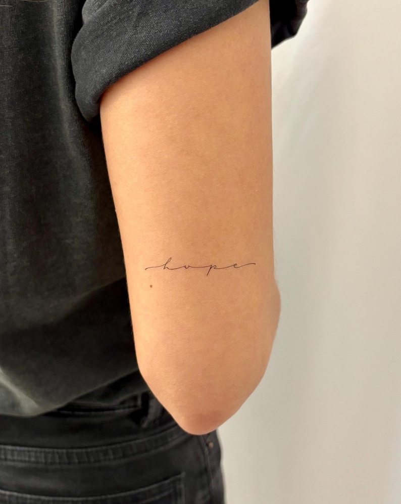 May include: A close-up of a person's arm with a simple cursive tattoo that reads "hope".