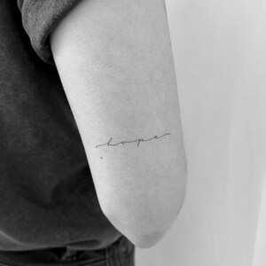 May include: A black and white photo of a person's arm with a simple cursive tattoo that says "hope" on the inside of their elbow.