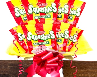 May include: A bouquet of pink and white candy in yellow and red packaging. The candy is wrapped in individual bags with the text "Squashies" printed on them. The bouquet is tied with a red ribbon.