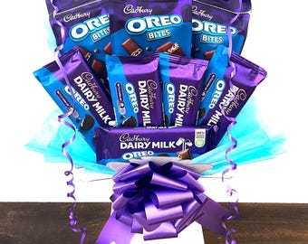 May include: A gift basket filled with Cadbury Dairy Milk Oreo chocolate bars and Cadbury Oreo Bites. The basket is wrapped in blue and white tissue paper and tied with a purple ribbon.